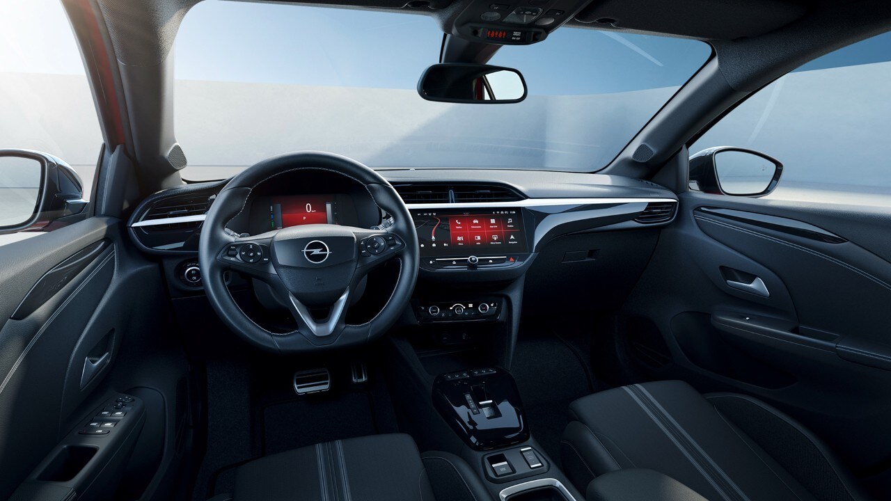 Intérieur noir de l'Opel Corsa Electric, vue latérale depuis le siège passager avec une femme en arrière-plan en chemise jaune