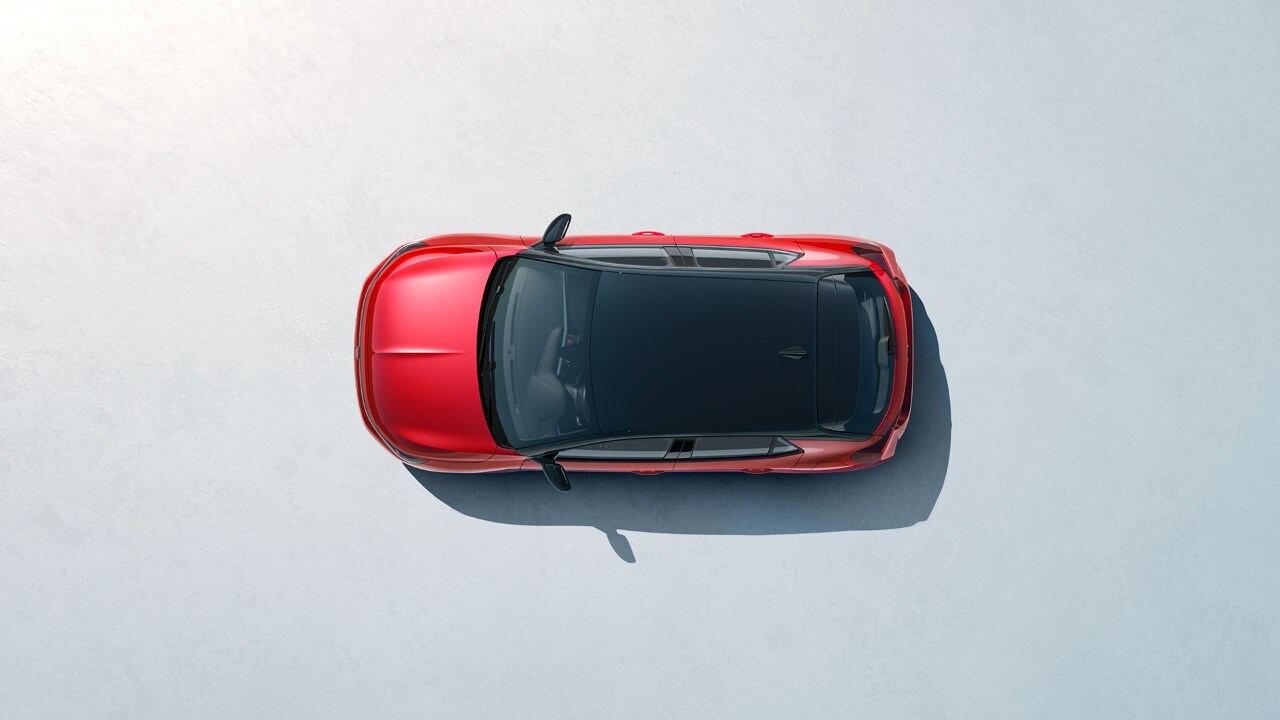 Femme debout à côté de la nouvelle Opel Corsa de couleur rouge avec toit noir et un homme qui monte par la porte du conducteur.